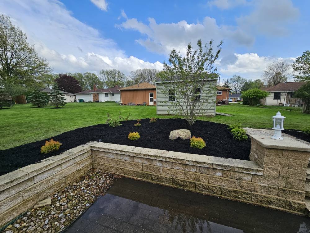Block seat wall forming a raised mulch bed with shrubs behind a paver patio