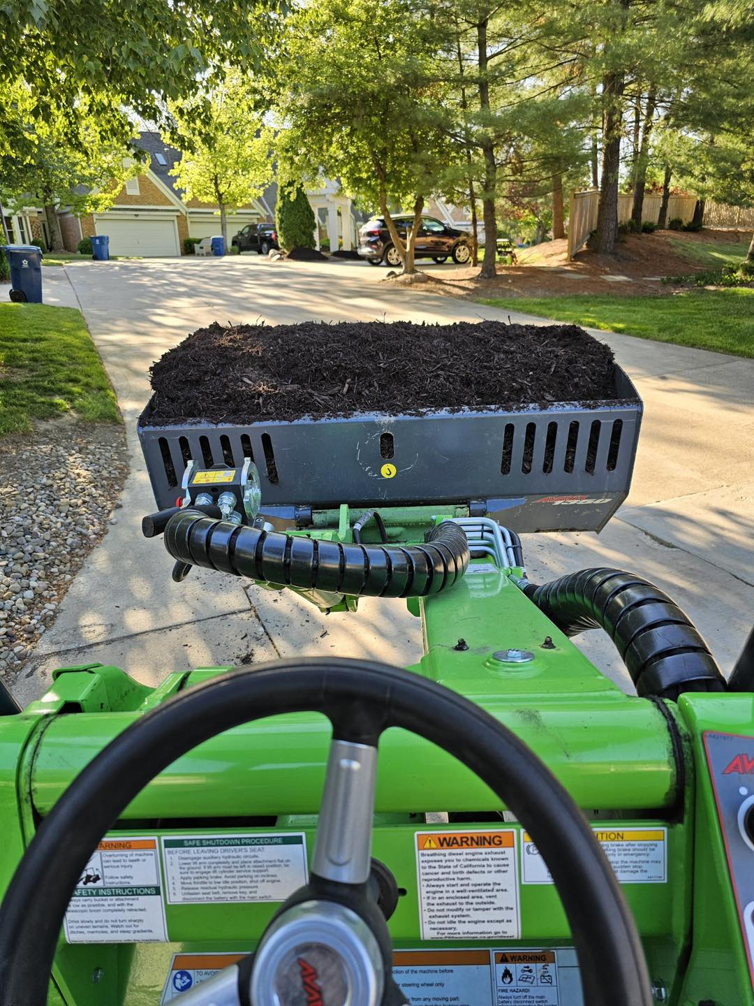 Compact loader carrying mulch up a residential driveway