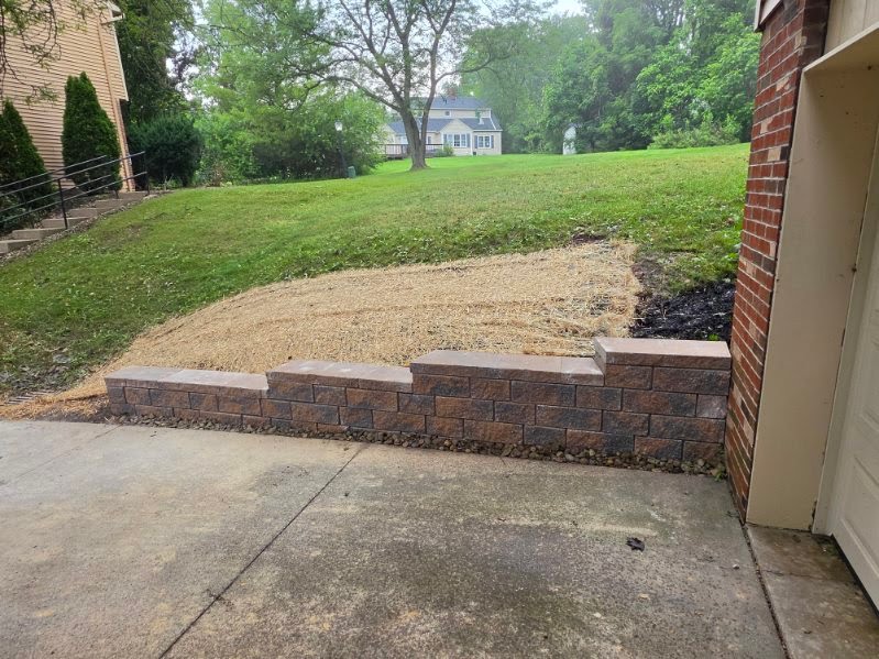Tiered block retaining wall along a driveway with fresh straw seeding above